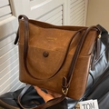 Sac seau vintage en cuir marron avec logo doré sur un siège en cuir noir - Café et Marron