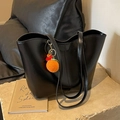 Minimalist black tote bag with orange crochet charm on elegant stone pedestal display - Black With Rabbit Pendant