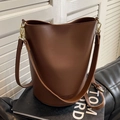 Bolso cubo de cuero marrón oscuro con correa ajustable y logotipo sobre libro negro - café