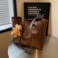 Brown leather tote bag with front pocket and plush bear charm on a silver table - Brown with Pendant