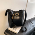 Classic black leather bucket bag with gold buckle and adjustable strap on a sofa - Black