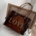 Brown transparent PVC tote bag with LOVE lettering and drawstring pouch on a rattan chair - Coffee