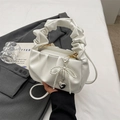 White ruched cloud handbag with pearl bow and heart charm displayed on a grey blazer - White