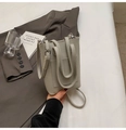 Gros plan d'un sac seau en cuir gris avec poche avant et logo élégant embossé - Gris