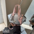 Silberne Metallic-Beuteltasche mit rosa Griffen und Ballon-Hund-Anhänger in der Hand - Silber