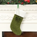 Green knitted Christmas stocking with faux fur trim and pom-poms on a white fireplace - Green