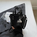 Mini black glossy bucket bag with silver balloon dog charm on a gray blazer background - Black With Pendant