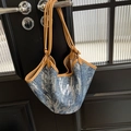 Blue denim tote bag with silver sequins and brown leather handles hanging on a black door - Brown