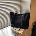 Minimalistische zwarte nylon tote bag met lange hengsels en logo op een wit boek - Zwart