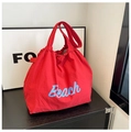 Primer plano de un elegante bolso tote de nailon rojo con texto Beach en azul - Rojo