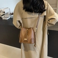 Braune Eimer-Umhängetasche aus Leder mit Narbenstruktur über einem beigen Trenchcoat - Khaki