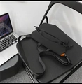 Detalle de bandolera negra minimalista con etiqueta naranja brillante sobre una silla - Negro