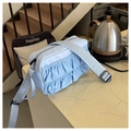 Detail view of light blue ruffled crossbody bag with adjustable wide strap on a chair - Blue