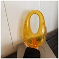 Detailansicht der bernsteinfarbenen Acryl-Handtasche mit Rundgriff und goldener Kettenkette - Gelb