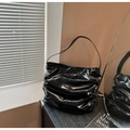 Détail du sac bandoulière en cuir verni brillant noir avec plis sur surface en bois - Noir