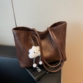 Dark brown leather tote bag with a cute white plush cloud charm on a black sofa - Coffee With Charms