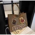 Dettaglio della borsa tote in tela marrone con ricamo orsetto e toppe con lettere retrò - caffè