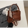 Dettaglio di una borsa a secchiello in pelle marrone con un foulard in seta sul manico - Marrone