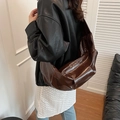 Chocolate brown pleated crescent bag in glossy leather, shown on shoulder for size - Brown