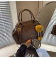 Detailed view of dark brown polished leather handbag with yellow plush monster charm - Brown