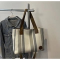 Detail of striped canvas tote bag with brown fabric handles and round leather logo patch - Gray