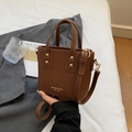Braune Leder-Tote-Bag mit Nieten und abnehmbarem Gurt, auf einem Bett präsentiert - Braun Ohne Anhänger