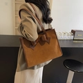 Caramel brown suede tote bag with large bow decoration shown in lifestyle cafe setting - Brown