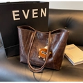 Detail of dark brown faux leather tote bag with plush charm on a black sofa - With Charm / Coffee