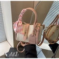 Detalle de bolso tipo cubo rosa y crema con cierre dorado y pañuelo de seda decorativo - Rosa