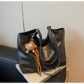 Close-up of black leather tote bag with gold logo and plush monster charm detail - With Charm / Black