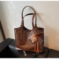 Detail of a dark brown leather tote bag with gold buckle straps and a plush monster charm - With Charm / Brown