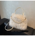 Detail of cream faux fur bag with pearl chain decoration on a leather surface - White
