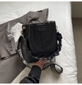 Detalle de bolso cubo negro con correa bohemia y asa trenzada sobre fondo de tela suave - Negro