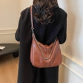Braune Hobo-Tasche aus Leder mit Silberkette und Ziernähten an einem Modell - Braun