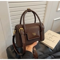 Detail of dark brown leather handbag with gold metal logo on a vintage flip-top square bag - Brown