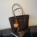 Dunkelbraune große Shopper-Tasche mit Bärenanhänger auf einer schwarzen Lederbank - Kaffeebraun