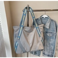 Dettaglio della borsa tote in tela grigia con tracolle ricamate blu e gialle su gruccia - Blu