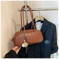Macro detail of a brown leather cylinder bag featuring a baseball glove charm and strap - With Baseball Pendant / Brown