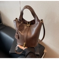 Detail view of coffee leather bucket bag featuring metal lock and tassel charm - Tan
