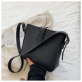 Bolso tipo cubo de cuero negro minimalista sobre cama blanca con accesorios modernos - Negro