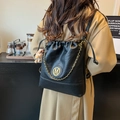Black bucket bag with gold chain, M logo, and teddy bear charm shown on model - With Charm / Black