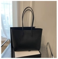 Detail view of a minimalist black leather tote bag with fine stitching on a metal cart - Black