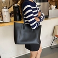 Bolso tote minimalista de cuero negro mate llevado por una modelo en una cafetería acogedora - Negro