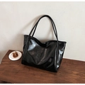 Borsa tote nera lucida in pelle sintetica con spalline lunghe su un tavolo di legno - Nero