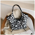 Details der flauschigen Leopard-Schultertasche mit schwarzer Lederschleife auf dem Stuhl - Schwarz-Weißes Leoparden-Plüsch-Stil / Schwarz
