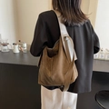 Braune Hobo-Tasche aus Wildleder mit breitem Gurt, getragen von einem Model im Café - Grün