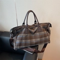 Brown checkered travel bag with leather handles and adjustable shoulder strap on a sofa - Brown
