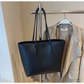 Detail of black matte leather tote bag with curved stitching on stylish clothing rack - Black
