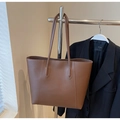 Detail of a brown leather tote bag with white contrast stitching on a minimalist metal rack - Coffee
