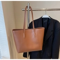 Brown faux leather tote bag hanging on a metal rack with a suit jacket background - Brown